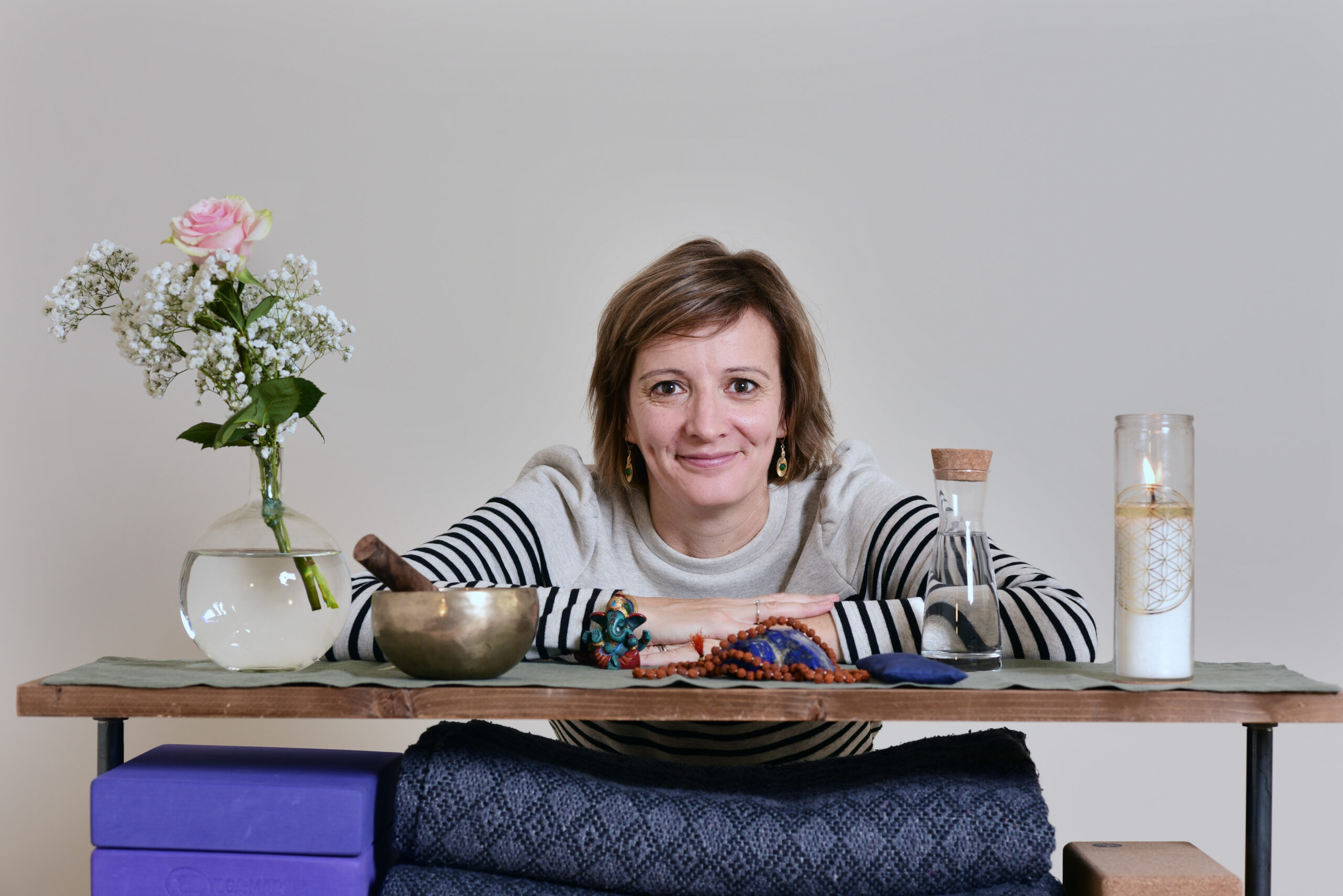 Audrey Favreau derrière une table avec des fleurs, un bol chantant et une bougie