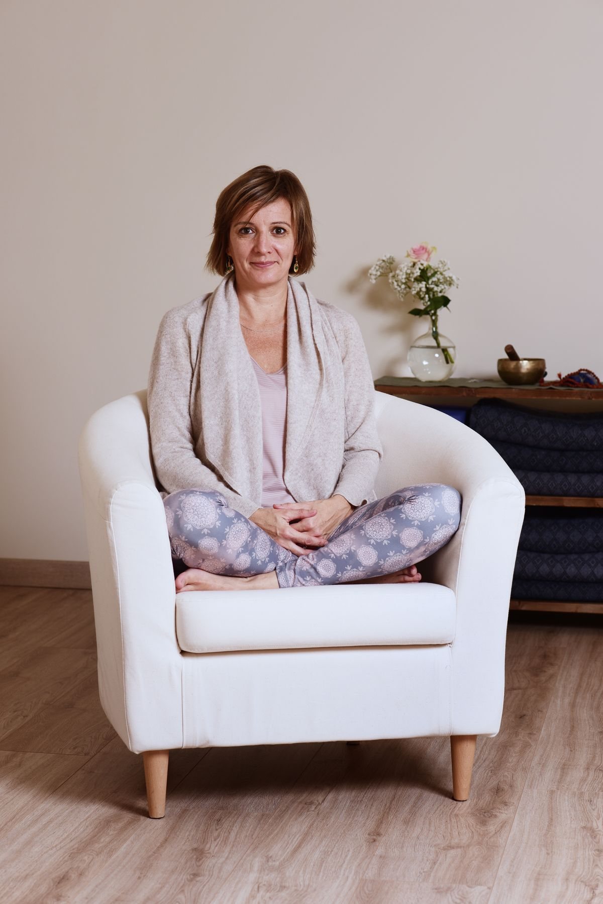 Audrey Favreau assise en tailleur dans un fauteuil blanc, dans son espace d’enseignement